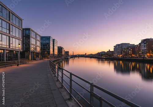 The tranquil beauty of a modern urban riverfront at twilight, with illuminated office buildings and a peaceful promenade