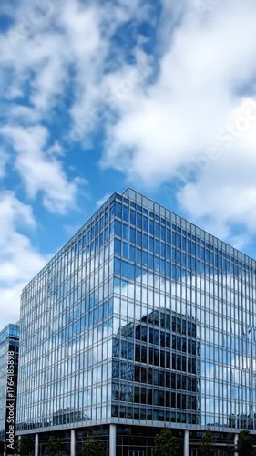 Modern glass building reflects a bright blue sky with fluffy white clouds, architectural marvel