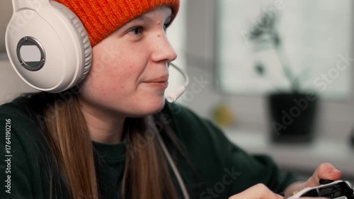 Young female gamer smiling and talking into headset during live game stream. Scene of online connection, gaming enthusiasm and social engagement through virtual space.