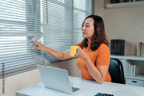 фотографія Woman taking a coffee break from her home office, peering out through window bli