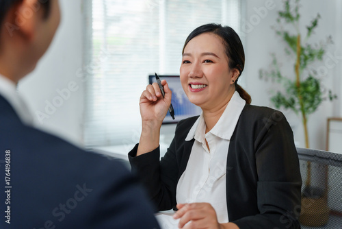 Smiling Asian business woman engaging in a productive meeting with a colleague, discussing ideas in a modern office environment