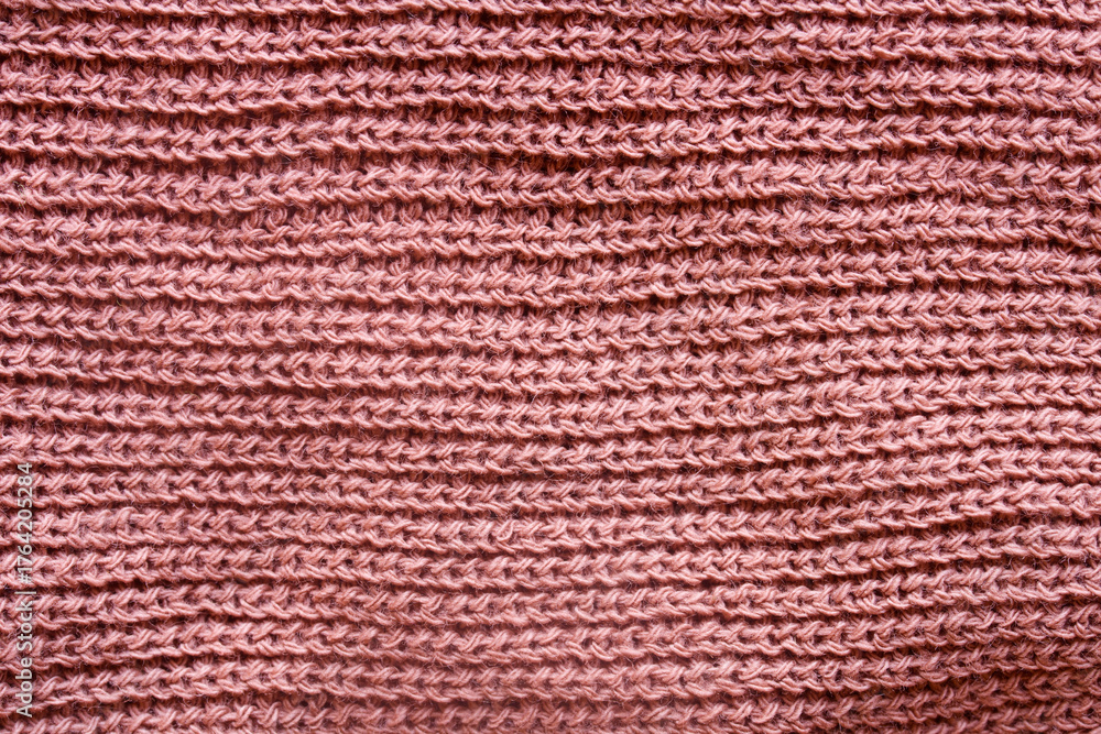 Fototapeta premium Close-up of soft pink knitted wool fabric with horizontal rows, showing texture and warmth in macro detail. Cozy textile background. Photo