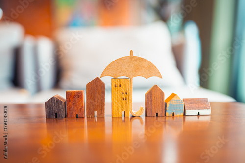 Wooden houses in a row with umbrella above, symbolizing home insurance, real estate protection, risk management, property coverage, housing safety, and financial security in real estate sector.