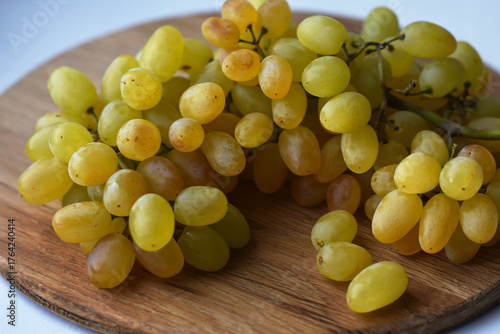 Large bunch yellow grapes on wooden plate. Food and summer background. Ripe grape Kishmish, sultana on wooden circle surface.