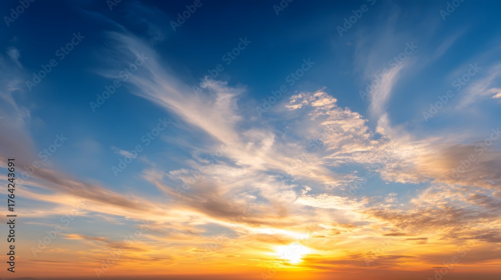 Obraz premium Vibrant golden hour sun illuminates high wispy clouds against a deep blue expanse.