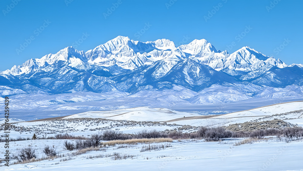 Fototapeta premium Wide winter view of snowy mountains under clear blue sky, bright white peaks rise above open valley with soft light and clean detail.