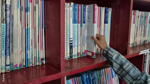 Hands of elementary school male students selecting books from library shelves. Pamekasan, Indonesia - Oct 22, 2025.