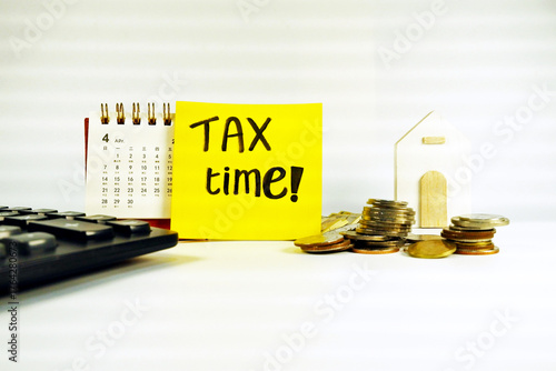 Tax Season: tax time reminder background digitally generated image stock photo copy space yellow note pad vertically stick on the calendar coins stacks foreground with calendar white block house