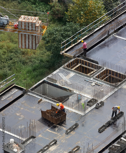 Workers prepare a grid of metal reinforcement for pouring concrete under construction of a monolithic apartment building