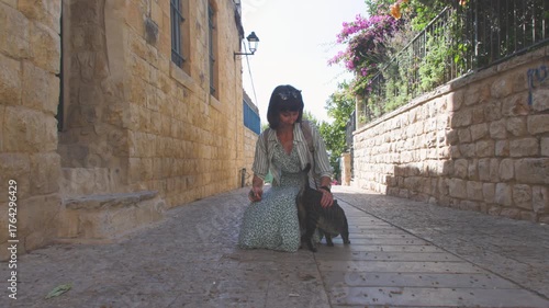 A female tourist pets a stray cat on the street. A stray cat on the street. A young woman pets a stray cat. The concept of good treatment of animals and helping them. Girl and cat.