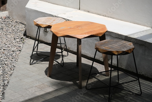 Set of wooden stools and a matching table with angular geometric tops, placed outside on a wooden deck in natural sunlight.
