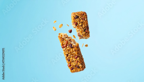 protein bar broken in half levitation. crunchy granola bar floating in mid-air with scattered oat flakes and nuts. Healthy snack muesli bar with chocolate flying on blue backdrop. cereal bar snack