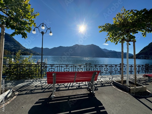Red bench by lake Lugano on a sunny day 