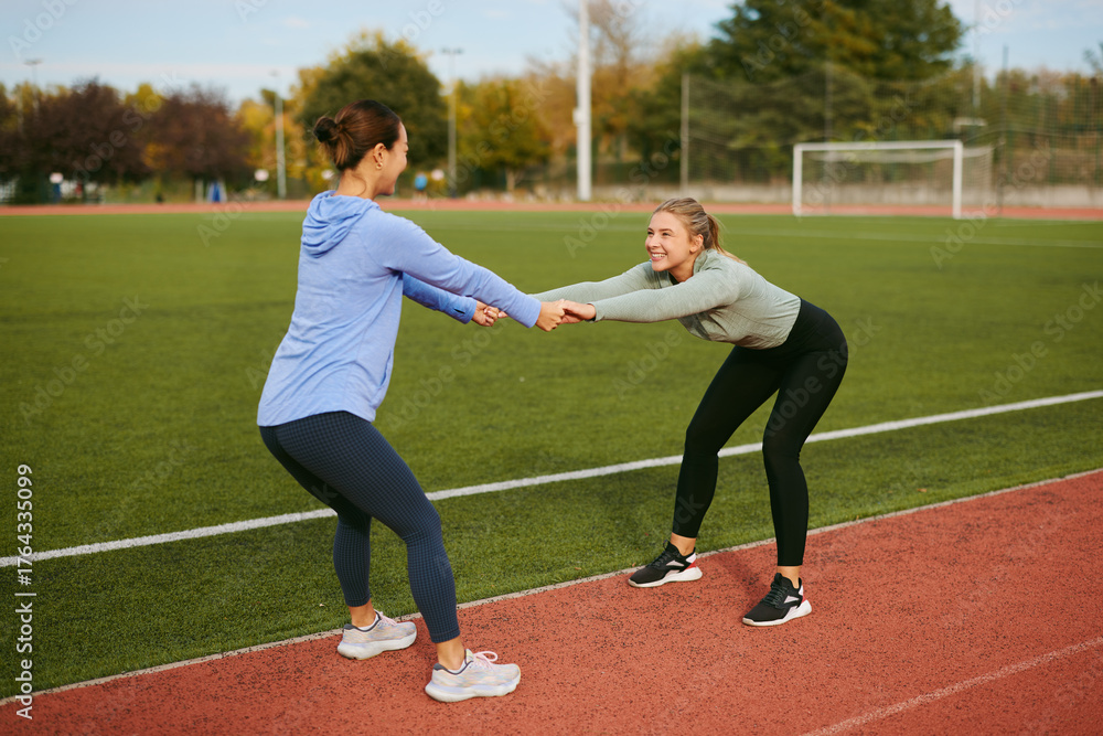 Obraz premium Women friends exercising stretching on sports field outdoors