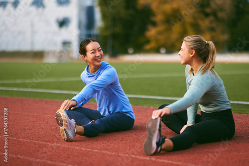 Women friends stretching on running track together