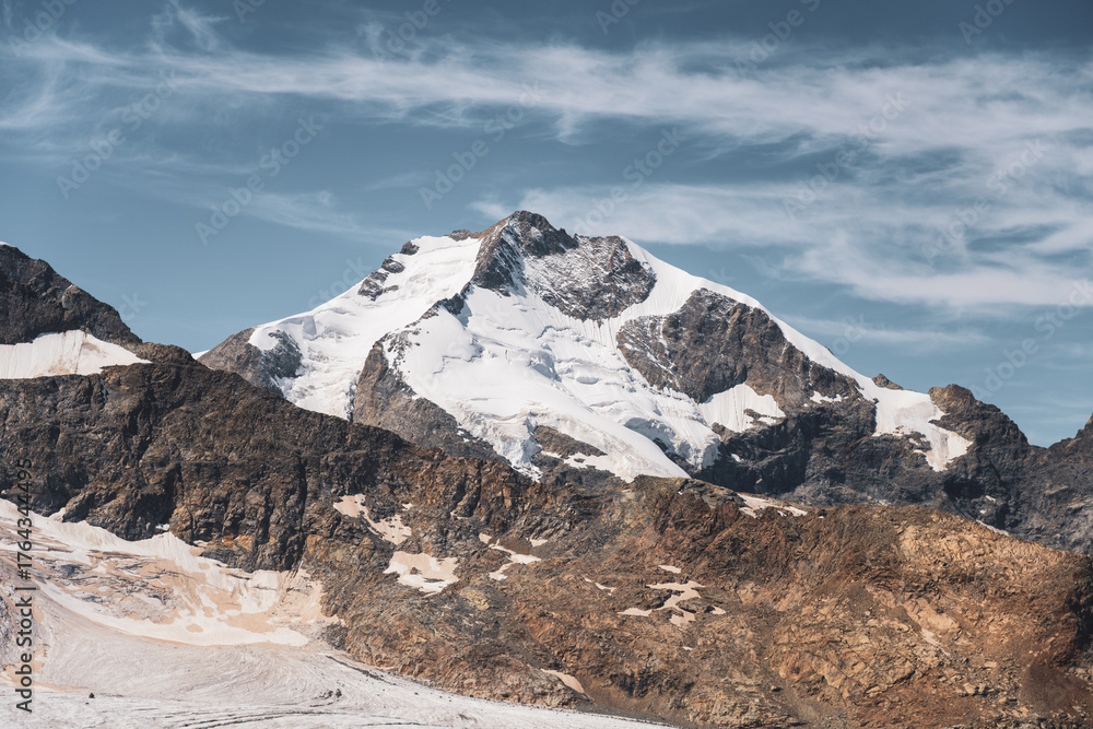 Obraz premium Piz Bernina towers in the Swiss Alps, showcasing its majestic glacier-covered summit against a clear blue sky. The rugged terrain and stunning natural beauty draw visitors year-round.