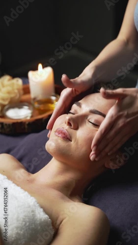 Woman receiving head massage in spa with candle and oil on wooden tray beside her, vertical footage