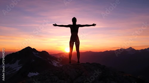 Silhouette of a woman with arms raised atop a mountain against a vibrant sunset