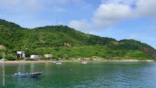 Fisherman navigates the tranquil waters of Puerto Lopez, Machalilla National Park Manabí Ecuador with lush green hills rising in the background under a vibrant blue sky dotted with fluffy white clouds