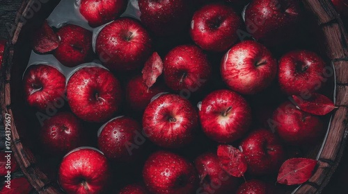 Bright red apples floating in a rustic wooden barrel filled with water. The apples are fresh, shiny, and vibrant, evoking a sense of harvest, autumn, and tradition