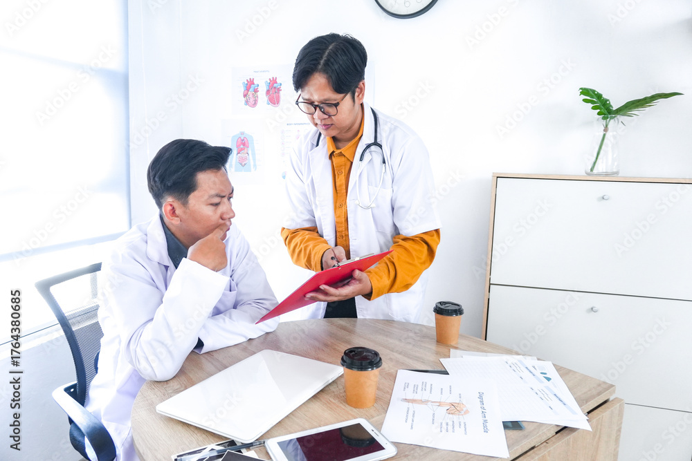 Obraz premium Focused Male Doctors Collaborating on Patient Case Reviewing Medical Charts Together in Bright Clinic Office