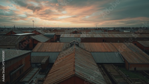 Warehouses stretching across city outskirts under sunset sky, with rusted roofs and smokestacks