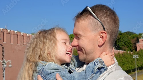 Little child girl rubs her nose against her father's nose outside