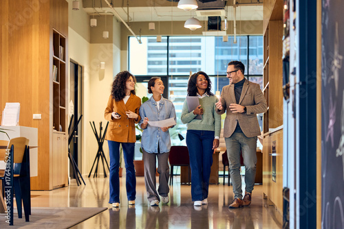 Diverse Group Of Colleagues Walking And Talking In Modern Office Hallway During Break