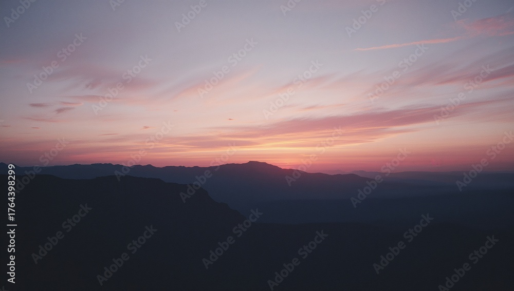 Fototapeta premium Displaying mountain ridges silhouetting under colorful dawn sky, with wispy clouds adding texture