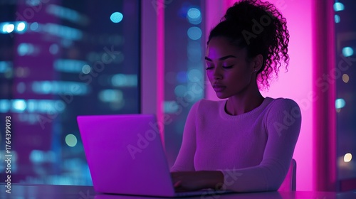 Woman working on laptop at night, with city lights in the background, illuminated by colorful neon lights.
