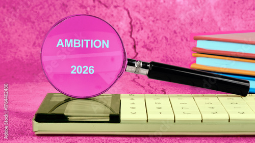 A magnifying glass emphasizes the word ambition for the year 2026, resting on a calculator along with vibrant notepads, showcasing a blend of motivation and organization