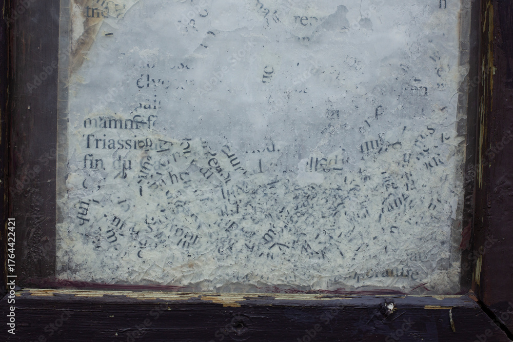 Obraz premium Close-up of weathered and partially erased text on a glass surface, framed by chipped dark wood. The faded black letters on a cloudy white background evoke age, decay, and forgotten information.
