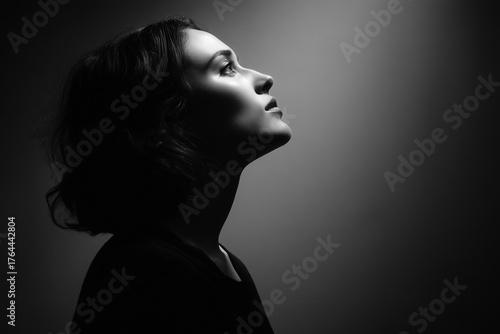 a dramatic black and white side portrait of a woman looking left and upward, strong contrast lighting from above, chiaroscuro style, minimal background, emotional and mysterious expression. horizontal