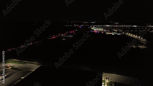 Flashing lights of emergency vehicles at night. Aerial backwards wide shot. Illuminated highway in american town with dark sky. Peaceful night scene in industrial area.