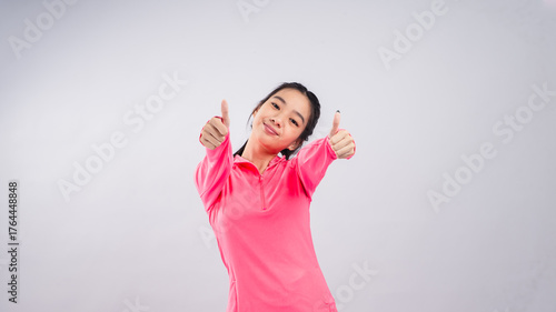 Asian woman in a bright pink long-sleeve sports shirt and black shorts standing confidently against a plain white background, smiling and showing a thumbs-up gesture straight toward the camera