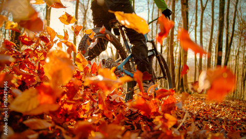 LENS FLARE, LOW ANGLE VIEW, CLOSE UP: Adrenaline mountain biker rides super fast along a forest trail, scattering fallen brown leaves in golden autumn morning light as he brakes through a curve.