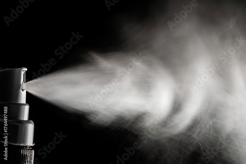 Perfume spraying from bottle on black background, creating a mist of fragrance in the dark studio shot