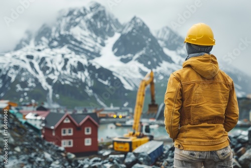 Worker overlooks construction site against a backdrop of mountains and snow in a remote location