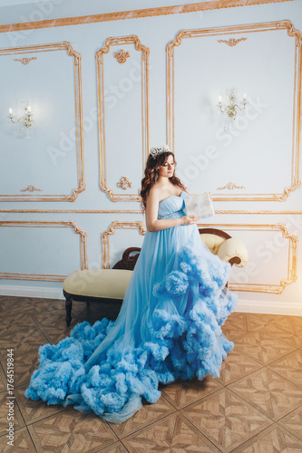 pregnant girl sitting on the floor in a lush blue dress. girl with dark hair wearing a crown.pregnant girl holding a gift. High quality photo