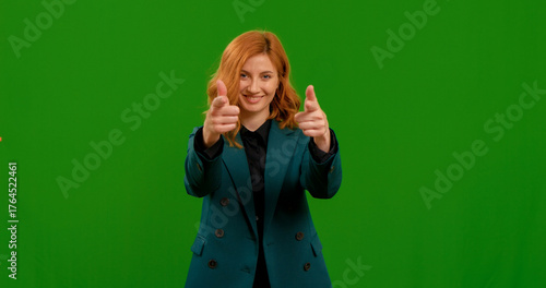 Cuadro en lienzo Woman points at the camera both hands and smiles over green screen studio