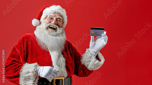 A cheerful Santa Claus in a red suit with a huge fluffy beard holds a credit card in his hands.