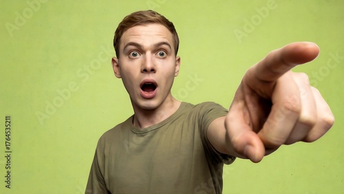 Shocked Young Man in a T-Shirt Pointing Emphatically Towards the Viewer or Side, With Wide Eyes and Open Mouth Against a Bright Lime Green Studio Background