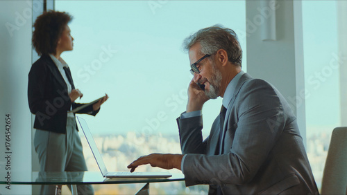 Obraz na plátne Business executive talking on a mobile phone and typing on a laptop with a femal