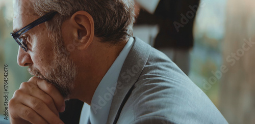 Thoughtful senior businessman with glasses and a beard, wearing a suit, intently focusing and contemplating a challenging idea or a complex problem in a professional setting
