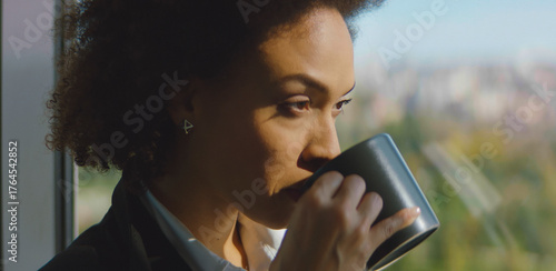 Billede på lærred Thoughtful woman sipping morning coffee by a window, gazing at the cityscape and