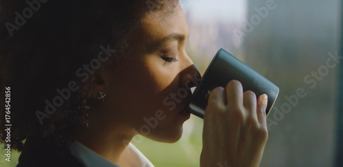 Foto Woman with eyes closed slowly sipping from a dark coffee mug, finding peace and
