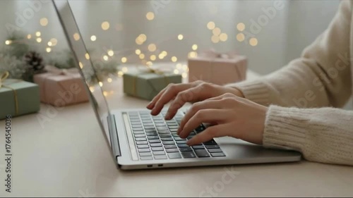 Online shopping for Christmas. A close-up of hands typing on a laptop keyboard. The background is decorated for Christmas with softly-wrapped gifts and twinkling lights.
