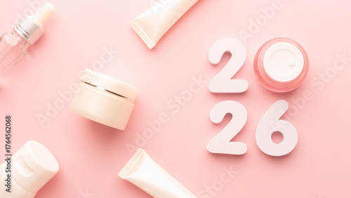 Best skincare products and cosmetic trends of 2026 concept. 2026 white number with lip balm, cream bottle, serum and lotion on pink background.