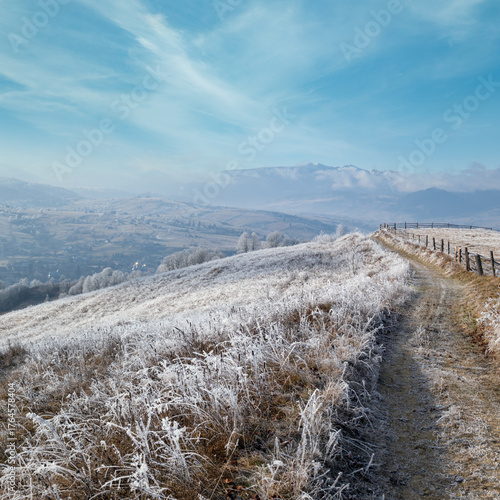 Winter coming. Last days of autumn, morning in mountain countryside peaceful picturesque hoarfrosted scene. Dirty road from hills to the village. Ukraine, Carpathian mountains.