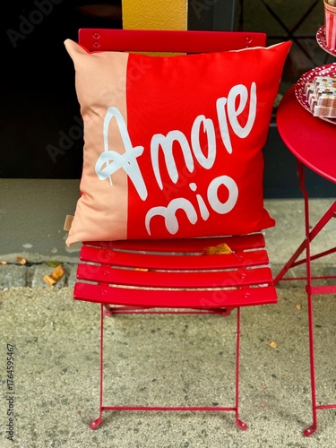 Red cushion with “amore mio” text on a red chair in outdoor cafe